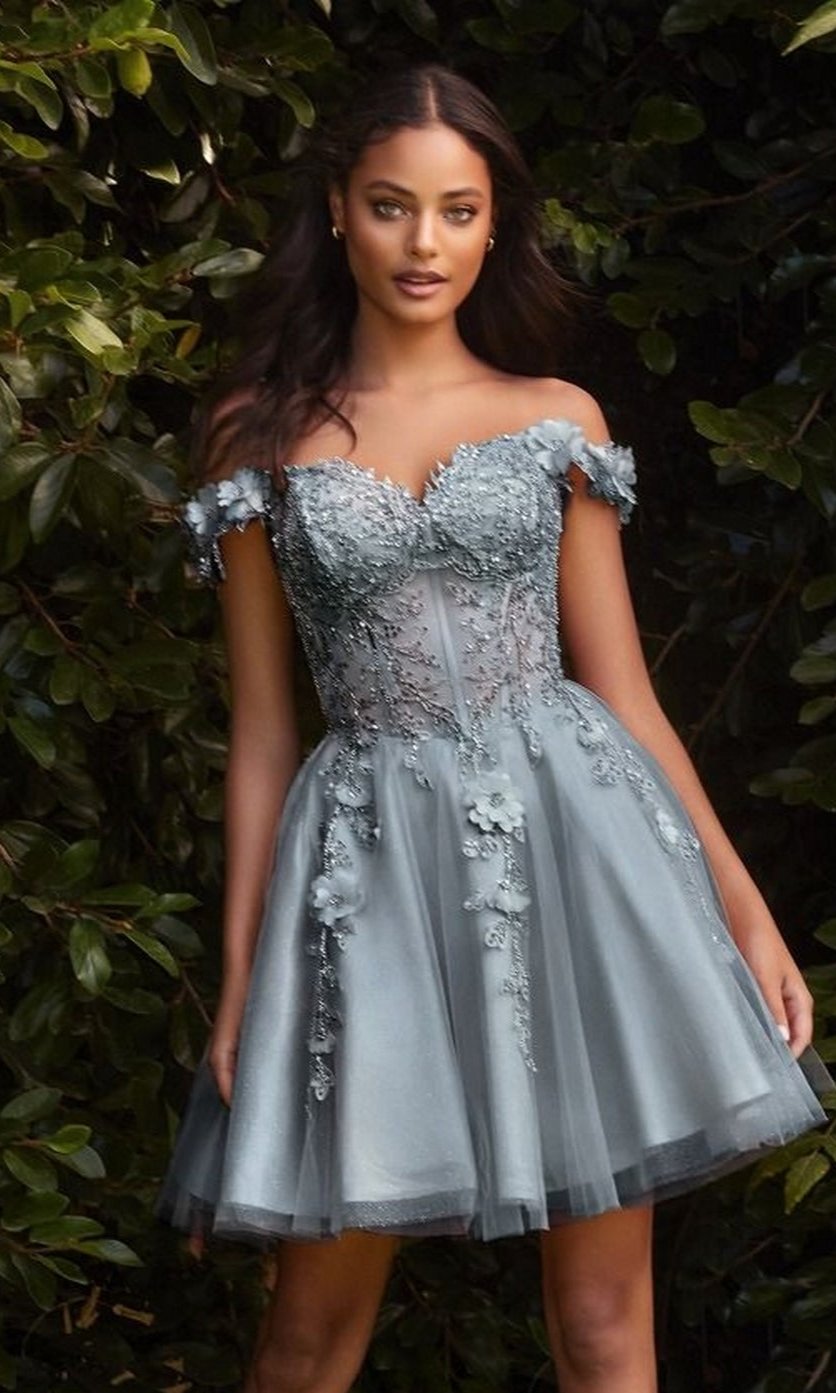 A woman stands outdoors in lush greenery wearing the Off-Shoulder Short Floral Homecoming Dress CD0194, a silver-gray, knee-length A-line dress with 3-D floral lace embellishments.